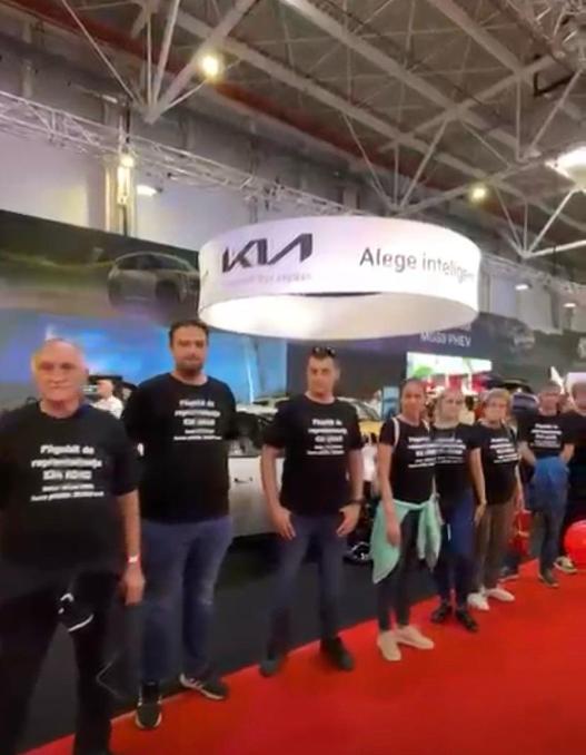 Protest la standul Kia de la Salonul Auto București. 20 de păgubiți protestează în tăcere in numele celor  130 de persoane care au rămas fără mașinile comandate VIDEO